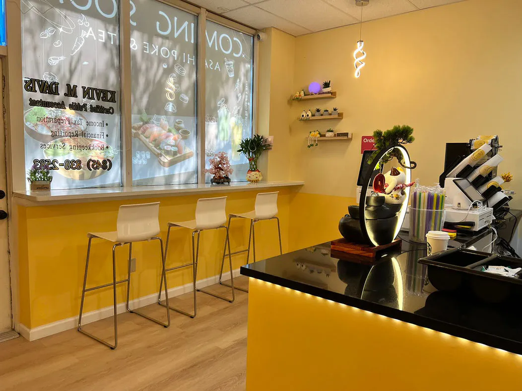 Bright yellow storefront with stools, decorative shelves, and service counter at Asahi Poke & Tea, a Bubble tea store in Beacon