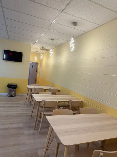 Light wood dining area with tables, chairs, and wall-mounted TV at Asahi Poke & Tea, a Bubble tea store in Beacon